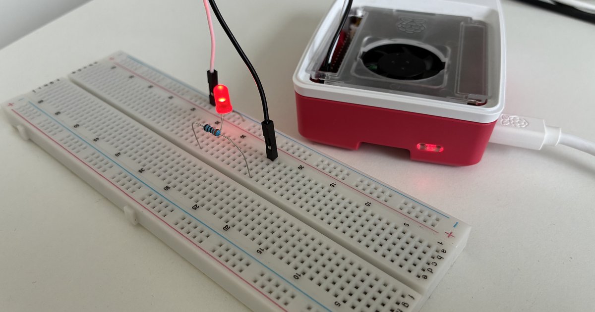 Een Raspberry Pi 5 in zijn behuizing met de statusled constant rood, naast een breadboard met een weerstand en een led op de GPIO-header