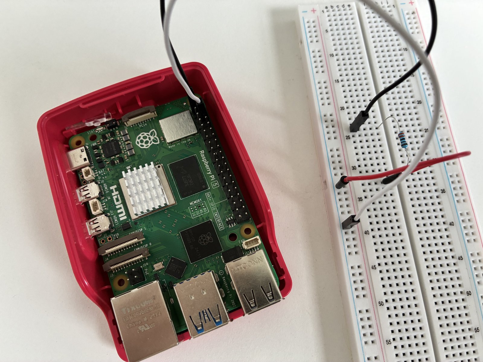 Bovenaanzicht van een kale Raspberry Pi 5 en een breadboard: een jumper van GPIO-pin 1 naar een weerstand van 330 ohm, de weerstand naar de massarail, en een jumper van de rail terug naar pin 6